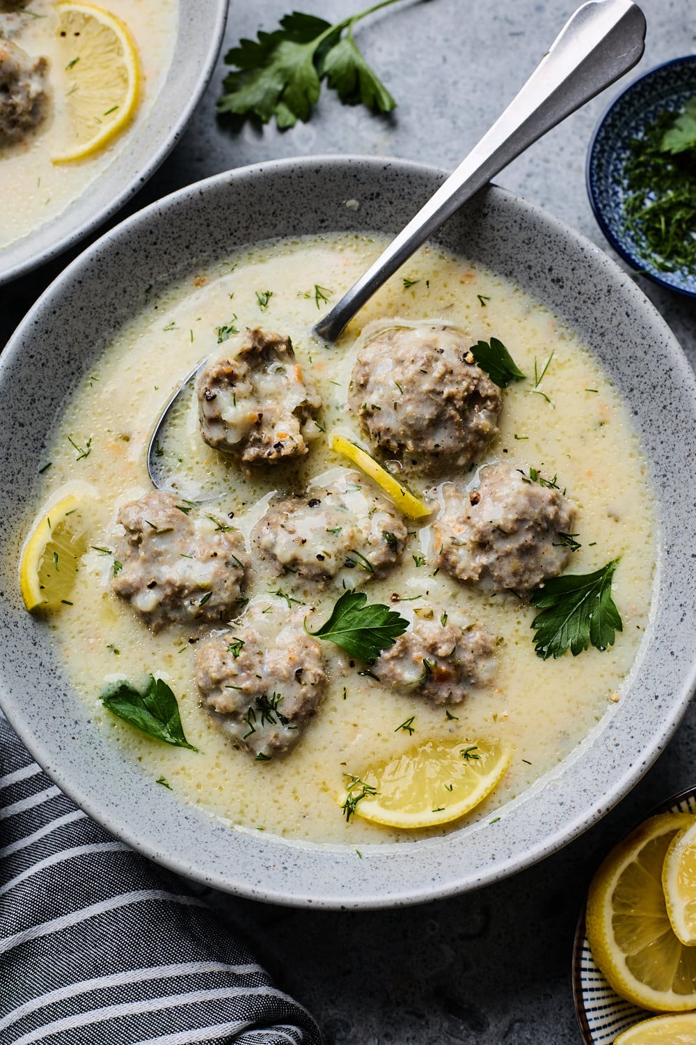 A bowl Youvarlakia Avgolemono with a spoon and a meatball cut into